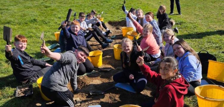 A group of school children pictured smiling excitedly at an excavation site in Downpatrick